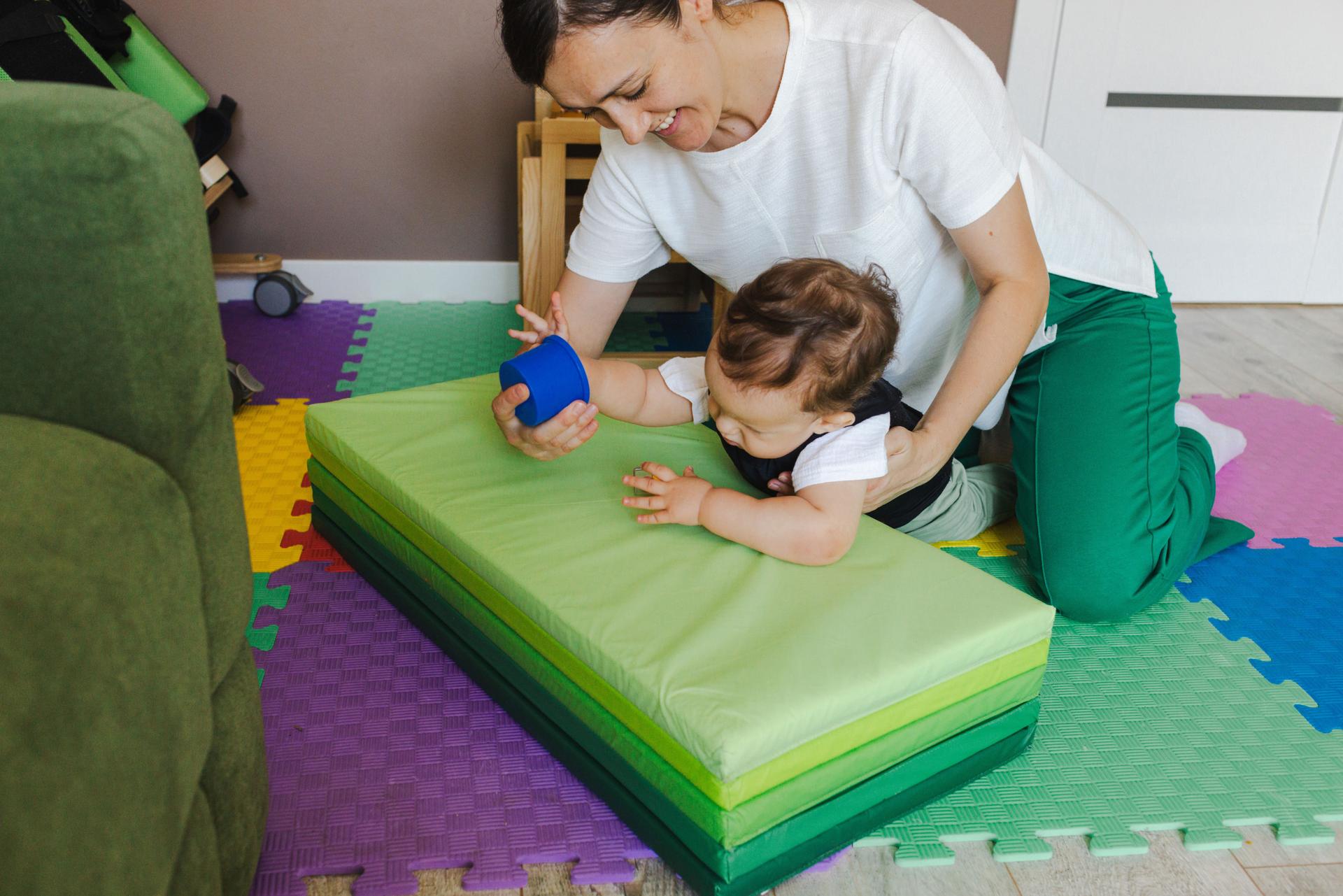 Young boy with hypotonia engages in physical therapy, supported by a his mother in a vibrant home rehabilitation space