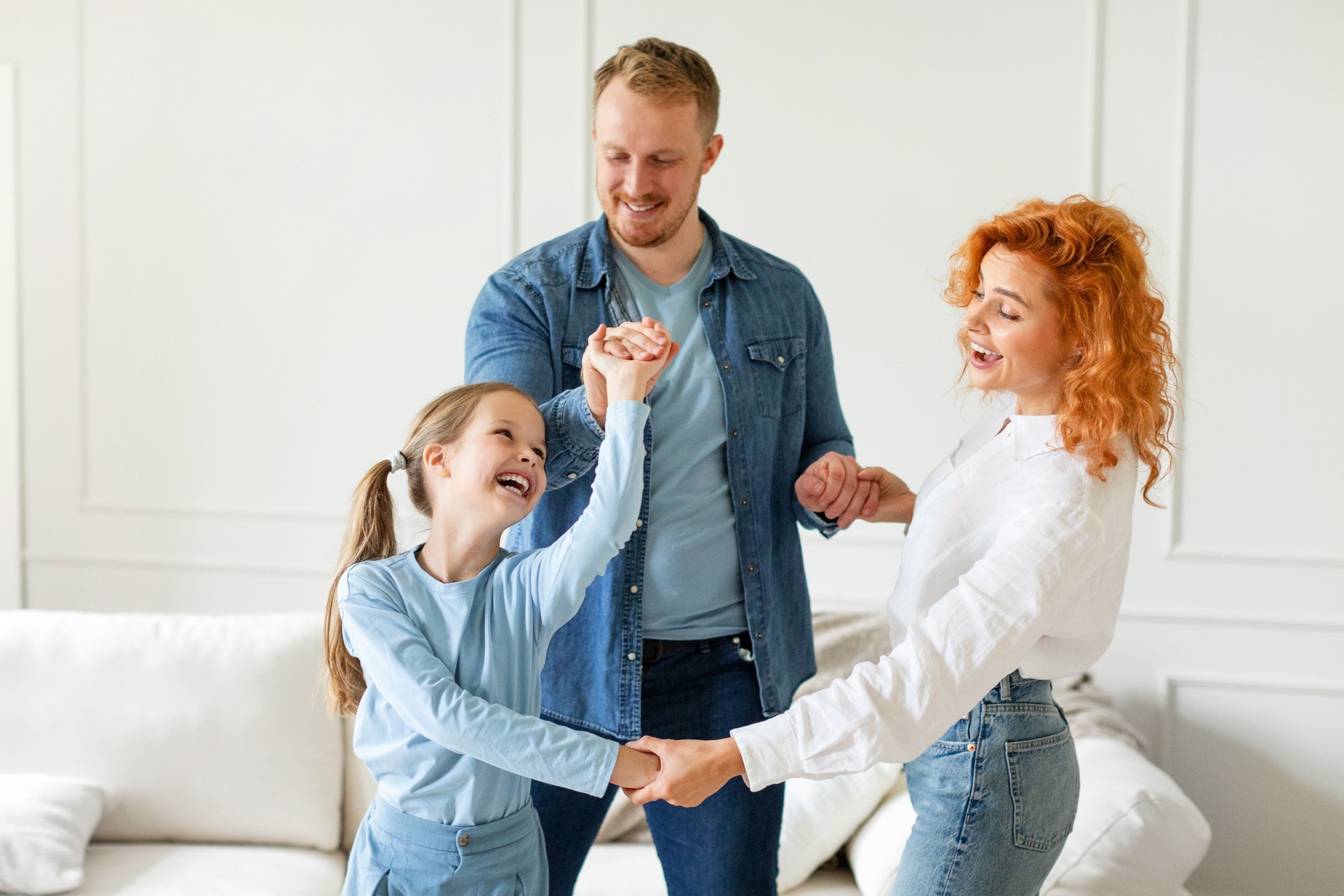 Family of three having fun, laughing and enjoying time at home, dancing together and holding hands, living room interior, free space